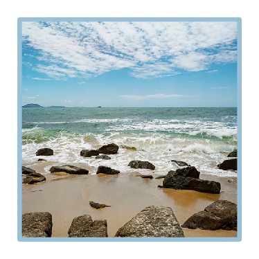 A landscape showing the sky and a beach with rocks on the sand. 